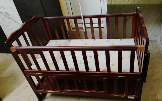 Wooden crib with a floral-patterned mattress cover on a wooden floor.