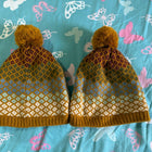 Pair of knitted hats with a pattern on a blue fabric background with butterfly designs.
