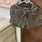 Leopard print shorts hanging on a hanger against a floral curtain background.