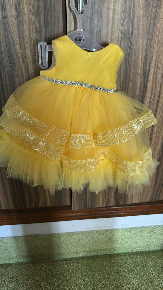 Yellow dress with a silver belt on a hanger against a wooden panel background