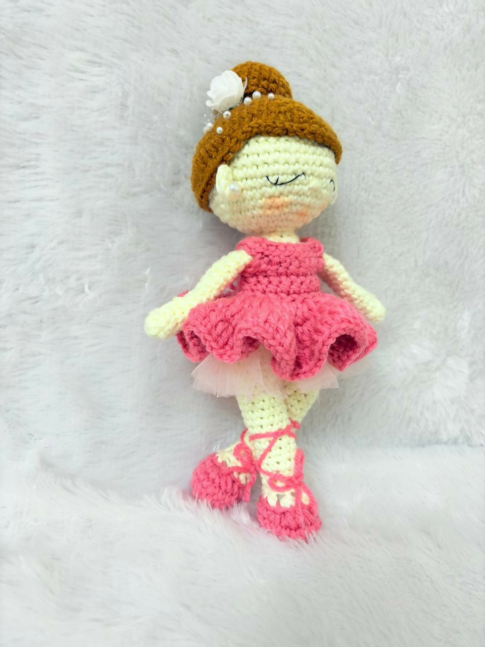 Crocheted doll with a pink dress and brown hat on a white background