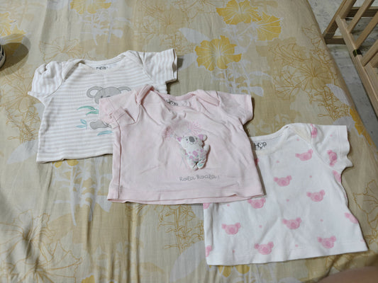 Three baby shirts on a floral-patterned bedspread