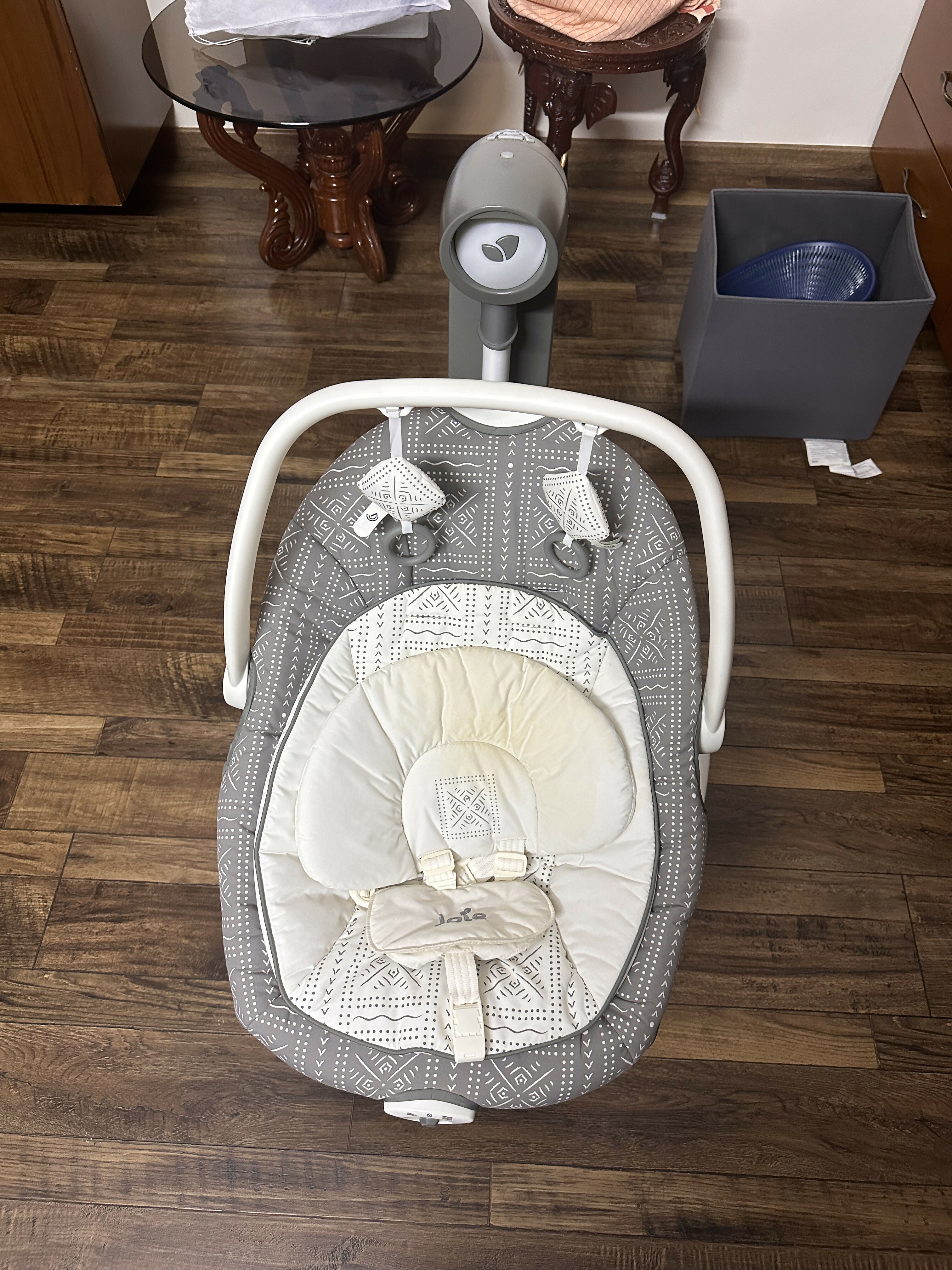Baby swing with baby clothes on a wooden floor in a room.
