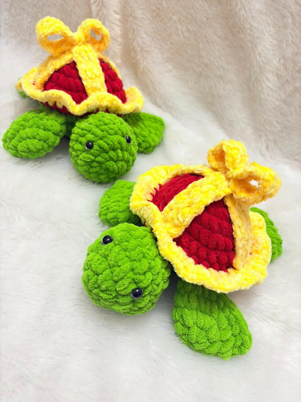 Two green crochet turtles with yellow and red shells on a white background