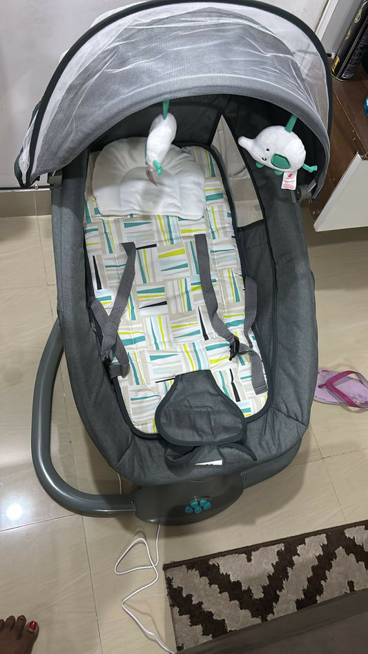 Baby swing with geometric patterned seat cover on a tiled floor.