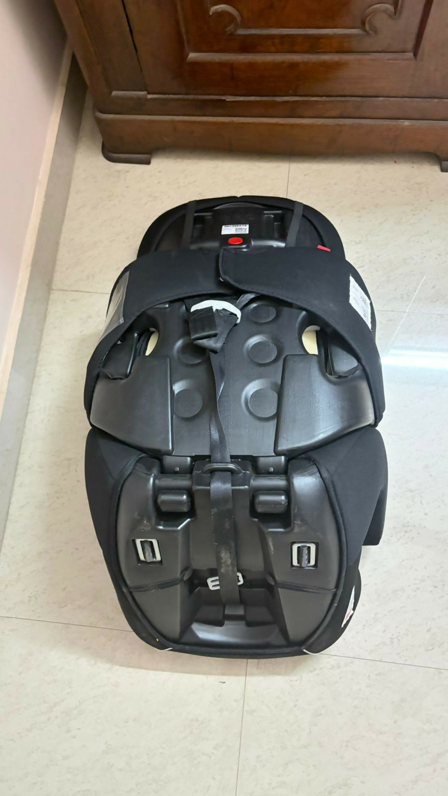 Black car seat on a tiled floor with a wooden piece of furniture in the background