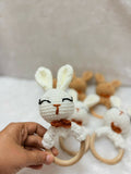 Hand holding a white crochet bunny with wooden teethers on a light background