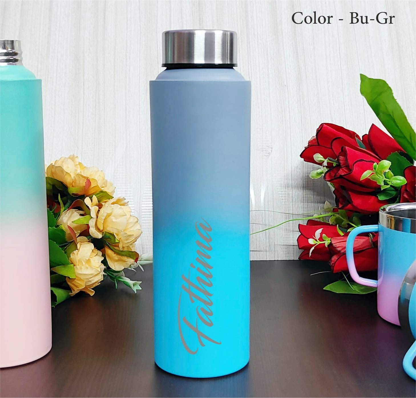 Gradient water bottle with floral arrangement on a wooden surface